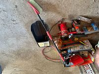 Photo showing battery charger with cables, red painted trailer hitches, battery tray, and handheld brush.