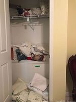 Closet shelf holding pillow and bed linens, various folded fabrics in white and floral designs.