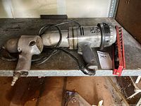 Black & Decker heavy duty impact wrench Model 625 with attached cable and trigger, placed on a shelf with a red socket holder nearby and a small impact wrench.