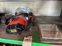 Black & Decker plunge router with attached power cord and red/black housing on green shelf with instruction manual beside it.