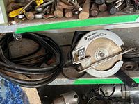 Photo showing Black & Decker Sawforce 100 circular saw with attached saw blade and long black power cord coiled beside it on shelf with other metal tools.