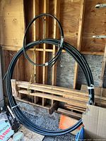Full view of large coil of black plastic pipe or tubing coiled and hanging in wooden framed area.