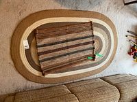 Two rugs, one oval brown-beige striped 61x38 and one small rectangular brown-beige striped 32x22 laid overlapping on carpet.