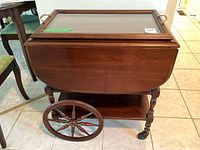 Front and side view of tea cart showing drop-leaf sides, glass top and decorative wheels