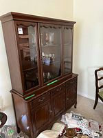 Full view of wooden china cabinet hutch with glass display doors showing interior shelves and bottom storage drawers and cabinets. Minor signs of wear visible.