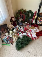 Photo showing various Christmas decor on floor including wreaths, fabric, mugs, DVDs, plush teddy bear, and Santa figurine.