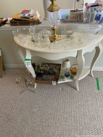 Front angle view of white painted demi table showing top surface and lower shelf with various glassware placed on and under it.