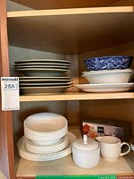 Top shelf of cabinet showing beige/tan plates and white plates with a blue and white speckled bowl.
