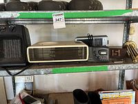 Shelf view showing cream horizontal fan, digital radios, wooden coin holder, brass mouthpiece, black box fan