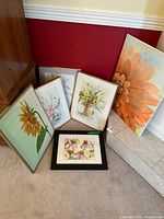 Six floral paintings grouped on carpet and hearth, showing variety and framing styles.