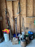 Wide view of tools including saws, broom, shovel, buckets and various containers inside garage