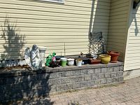 Wide shot of garden lot items arranged on stone ledge and ground showing statue, planters, watering cans, trellis, and wooden stand