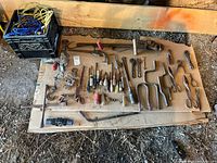Hand tools laid out on cardboard, including wrenches, saws, clamps, non-powered hand drills, scissors, screwdrivers, and other vintage implements.