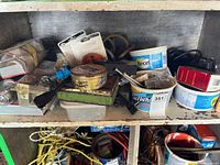 Shelf with various boxes, plastic containers, and tins containing mixed nails, screws, rope, and miscellaneous hardware items.