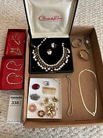 Overview of assorted costume jewelry including boxed pearl-like bead and gold-tone necklace set with earrings and ring, two red velvet boxes with chain necklaces, various pins and brooches, bracelets, and three watches.