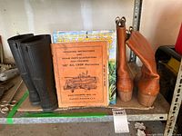 Photo showing a pair of black rubber boots, a pair of brown Kodiak leather work boots with wooden heels, and several agricultural reference books including a vintage Allis-Chalmers crop harvester manual and a tractor magazine.