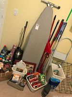 Photo showing ironing board, Shark vacuum, cleaning tools, and baskets with cleaning and laundry supplies
