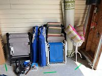 Five folding lawn chairs in various colors and styles stacked near a wall, assorted pet dog supplies including collars, leashes, and a book on the floor.