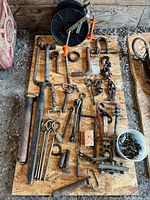 Wide view of lot showing various metal rods, hooks, clamps, cable reel, and other hardware items laid out on plywood board.