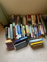 Photo showing multiple rows of books stacked in mixed formats including hardcover, paperback, and spiral-bound with visible wear on some covers.