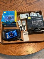 Lot contents showing two Nikon Coolpix boxes, one Nikon Coolpix S32 camera in blue, two Kodak EasyShare CX7430 cameras in silver, and various accessories including batteries and chargers.