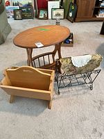 Photo showing three magazine racks and an oval wooden side table on carpet with paintings in background