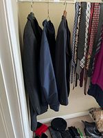 Photo showing three men's suit jackets or coats hanging and several men's neckties to the side.