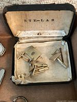 Metallic cufflinks in vintage black box labeled STE-LAR, showing a total of six cufflinks and a pair of shirt collar clips.