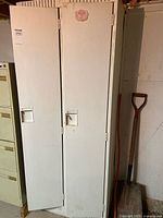 Full front view of the two-door white metal locker showing the two narrow doors, handles, and a faded sticker.