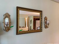 Photo showing the rectangular gold gilded framed mirror reflecting part of an interior room.
