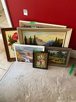 Six framed paintings shown stacked and leaning against a red wall, varying sizes approximately 9x7 to 16x19 inches, depicting landscapes, floral and pastoral scenes.