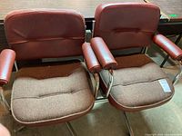 Two vintage office chairs side by side showing brown vinyl backs and armrests, brown fabric seats, metal frames with some rust, one chair with caster wheels, the other without wheels.