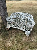 Full front view of the small cast iron bench showing ornate decorative backrest and weathered paint
