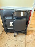 Three folded black folding card tables leaning against a wall, showing their metal legs and black tabletops.
