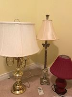 Three table lamps with different bases and shades, placed on floor against a yellow wall.
