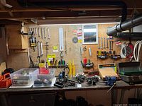 Wide view of workbench with various hand tools hanging on pegboard, small tools and electrical items on bench, and vise on the right