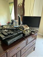 Photo showing Insignia 19-inch TV, DVD player, VHS player, remotes, CDs and cables on dresser surface with mirror background.