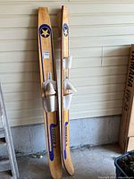 Pair of vintage Starfire 2 wooden water skis leaning against wall showing full length and bindings.