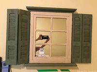 Full view of the wall mirror with green shutter-style doors open on both sides, cream/white framed central windowpane mirror.