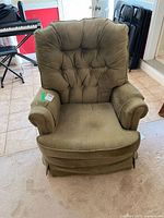 Full front view of the olive green Whole Home swivel rocker chair showing cushioned back with button tufting, rounded armrests, and the seat cushion in place.