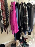 Photo of women's assorted clothing hanging on rack, including scarves, ties, jackets, and long sleeve blouse in purple.