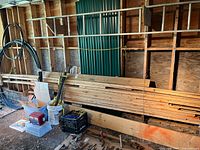 Wide view of assorted wood planks and boards horizontally stacked in a storage shed, some bundled with twine, showing various sizes and thicknesses.