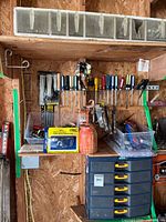 View of assorted screwdrivers and wrenches organized on a pegboard above a wooden bench, with additional hardware items stored in bins and containers.