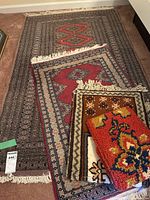Four nested area rugs laid on carpet; visible color variations and designs ranging from geometric to floral patterns.