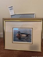 Two stacked framed prints leaning against wall; front shows wood duck print in gold-tone metal frame