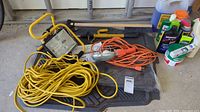 View of the yellow and orange halogen work lights with long extension cords, automotive mats underneath, and various cleaning products to the side, along with a yellow-handled brush and white tape roll.