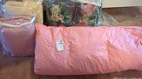 Pink single bed duvet folded and two cushions in plastic packaging with floral pattern cushion behind