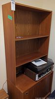Full view of the wooden bookcase showing shelf layout and cabinet base with items placed on the shelves.