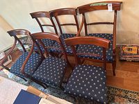 Front angle view of six matching wooden dining chairs with blue patterned upholstered seats arranged on hardwood floor near a rug.