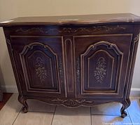 Front view showing carved floral decoration on door panels and ornamental feet of wooden hall cabinet